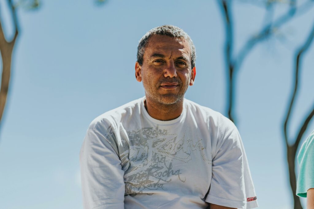pexels photo 13872504 13872504 Casual portrait of a middle-aged man sitting outdoors under a bright blue sky.