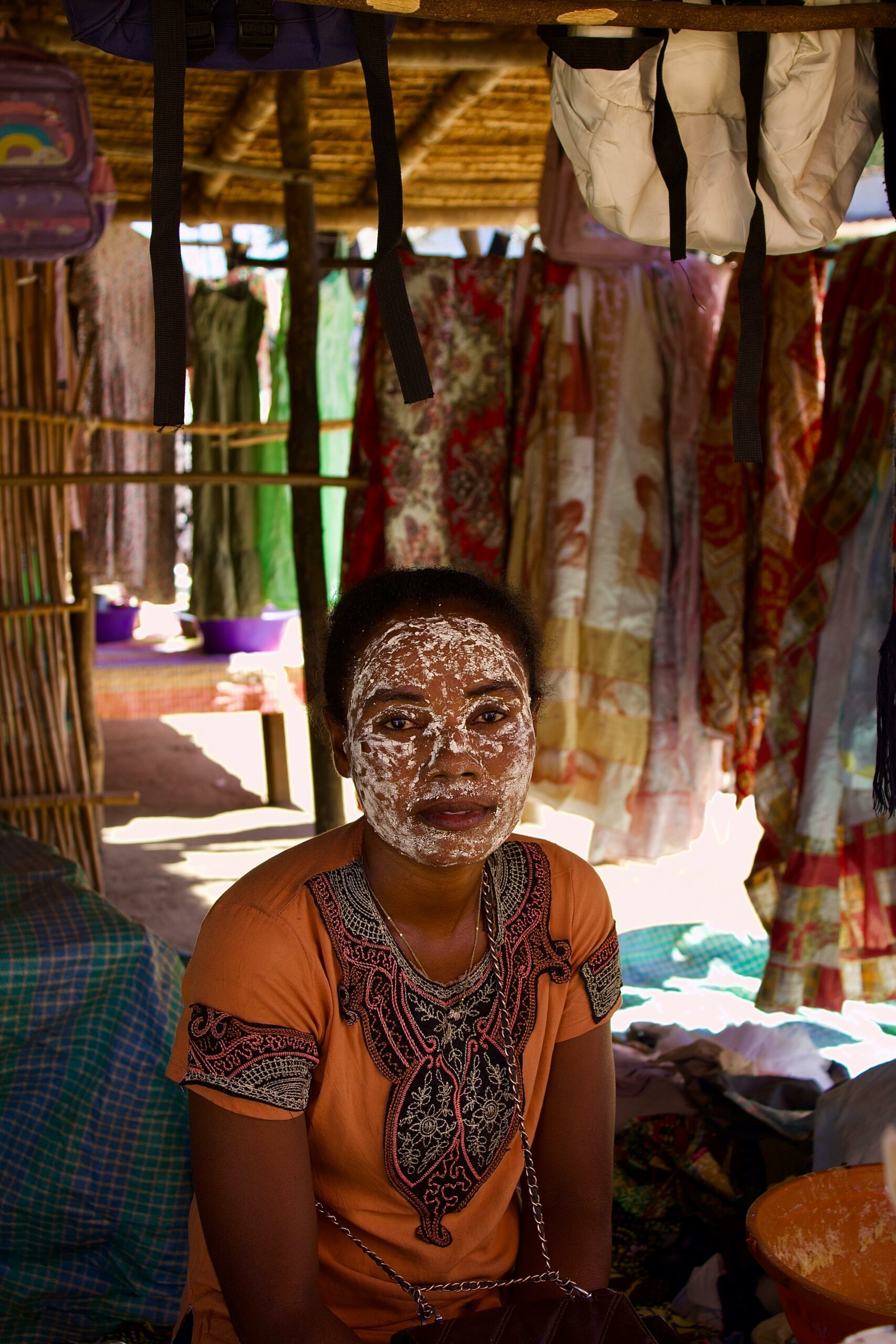 Top 5 des activités incontournables à Madagascar Woman with a traditional face mask in a Malagasy market stall displaying vibrant fabrics.