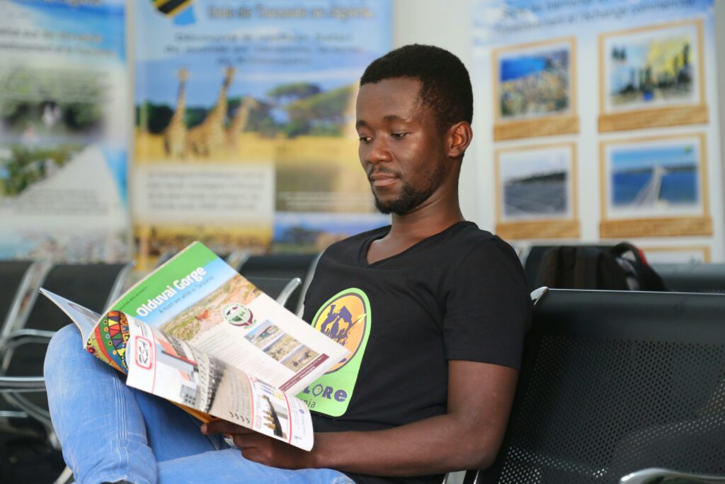 pexels photo 9718807 9718807 A man sits indoors reading a brochure about Olduvai Gorge, in a modern waiting area.